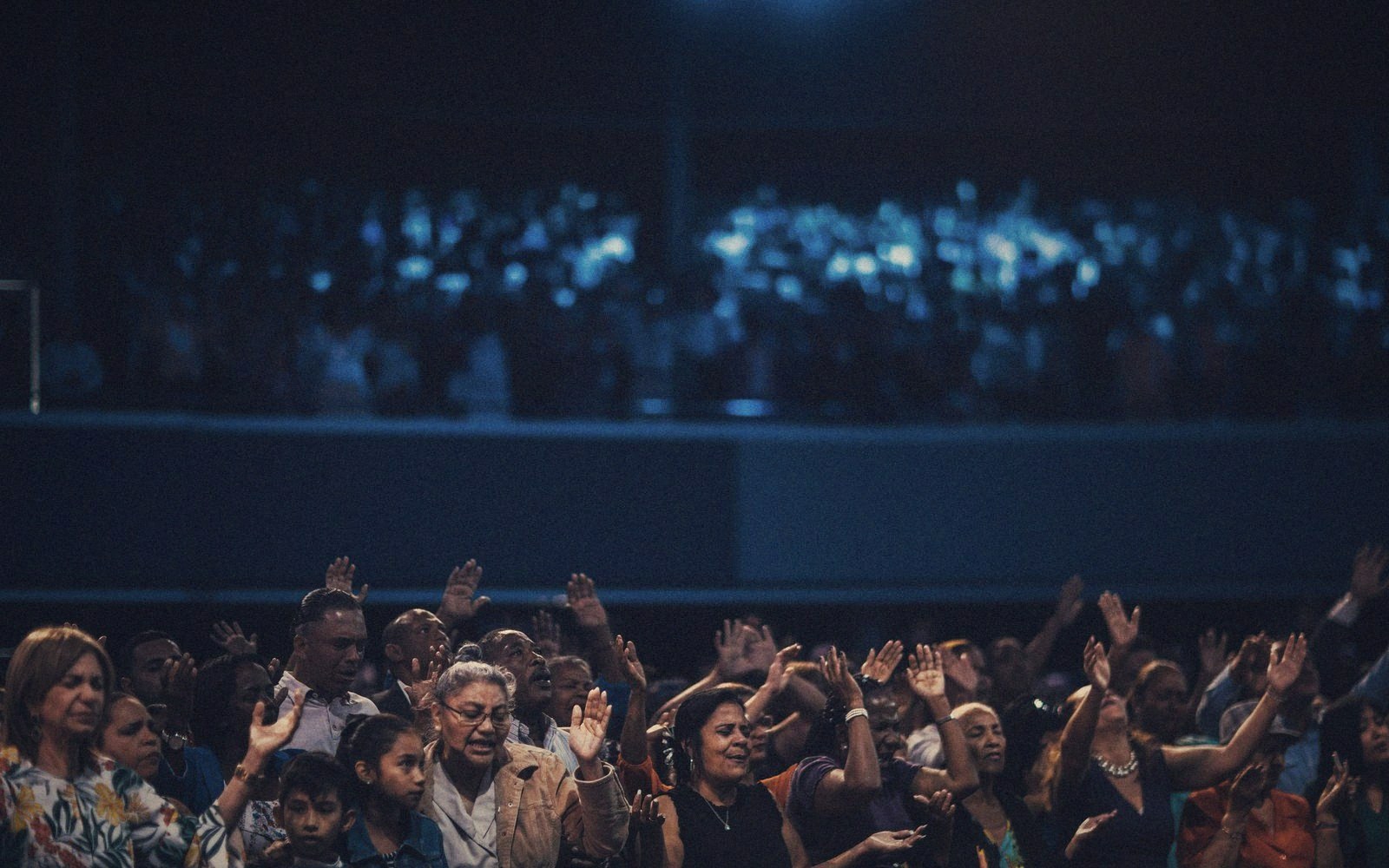 Crowd raises hands together during a nighttime gathering in a packed arena