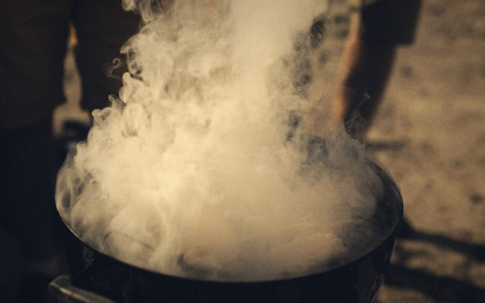 Thick steam billows from a large pot as someone stands nearby outdoors