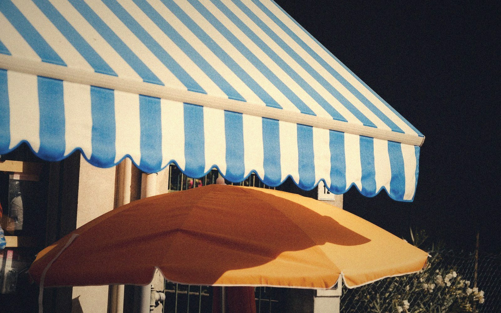 A blue and white striped awning above an orange patio umbrella at night