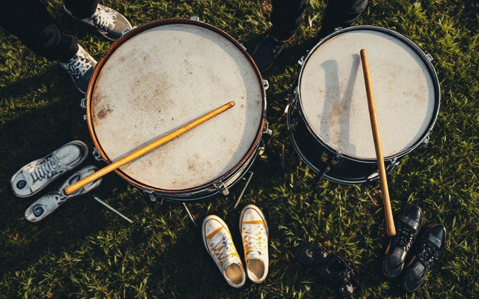 Overhead view of two snare drums with drumsticks surrounded by sneakers on grass