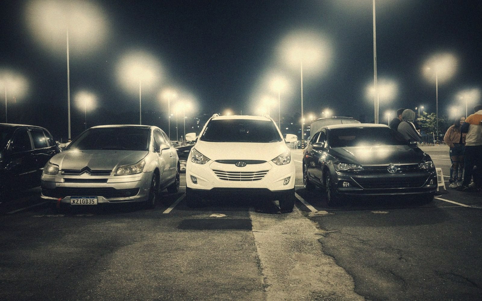 Rows of parked cars illuminated by tall stadium lights in a nighttime parking lot