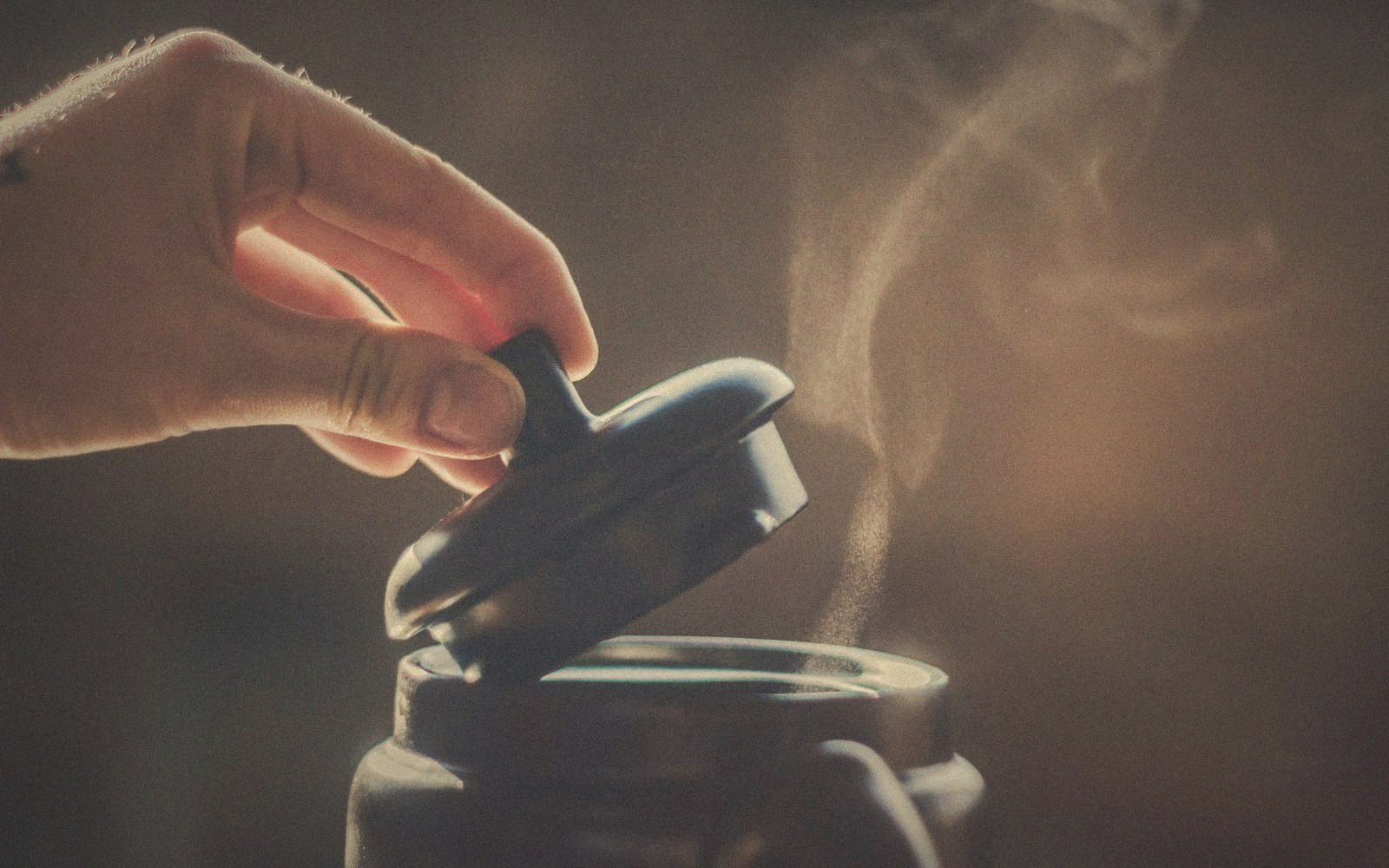 Hands lifting a lid in a cloud of steam